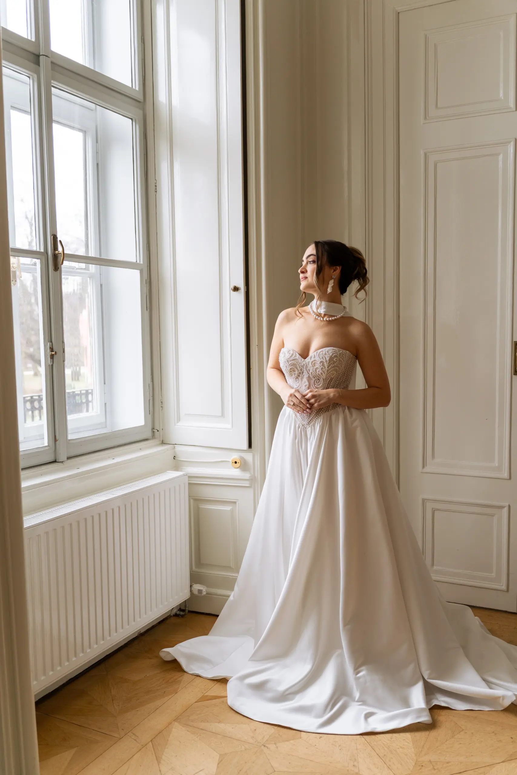 Braut steht beim Getting-Ready mit ihrem Brautkleid bei einem schönen Fenster im Europahaus Wien.
